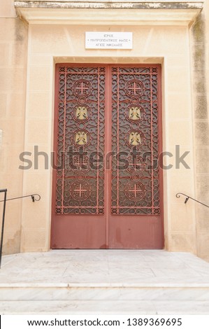 Sign above the metal door with Greek words which translate to "Greek Orthodox Church of Saint Nicholas"