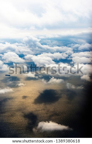 Clouds from a window of a commercial plane with sea and some ships over the sea.