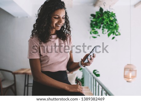 Cheerful hipster girl feeling excited of chatting with friends using free 4g internet on cellular phone, happy female blogger watching video via media app on smartphone during spare time indoors