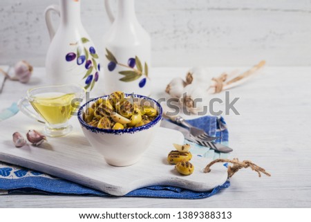 Grilled olives with garlic, olive oil and spices on white rustic wooden background