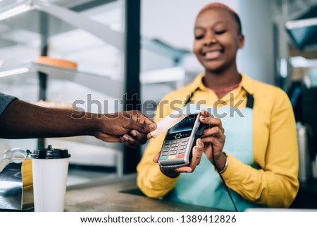 Hand of anonymous black man holding contactless credit card near payment terminal while buying takeaway food in modern cafe