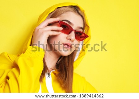 Pretty young girl with red glasses, and yellow hood on.