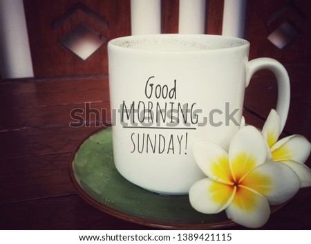 White mug of coffee with good morning sunday greeting on it and beautiful Balinese frangipani flowers arrangement. Happy Sunday! Have a relax sunday.
