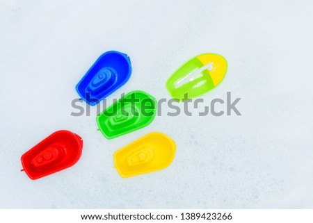 Plastic multicolored toy boats on foam bath. Top view. Children toys for bathroom.