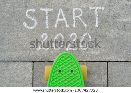 Start 2020 written in chalk on gray sidewalk, skateboard before the text