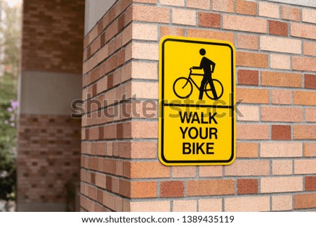 Close up on a "Walk Your Bike" sign on a brick wall, along a pedestrian walkway, with space for text 'on the left and right