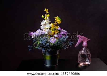 White and yellow flowers in a pot and a water bottle. On black background.