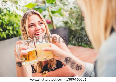 Cheerful blonde with friend at the bar drinking beer and celebrating in friendship toasting the glasses and having fun together - happy people celebrate with friends