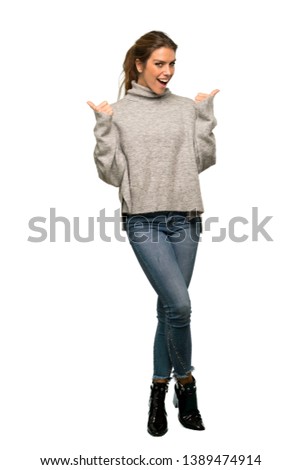 A full-length shot of a Blonde woman with turtleneck giving a thumbs up gesture and smiling over isolated white background