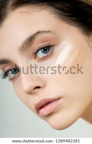 Young woman applying three color samples of facial foundation cream at her face. Beauty model with perfect fresh skin and long eyelashes cares about her skin at home. Skin Care Concept. Royalty-Free Stock Photo #1389482381