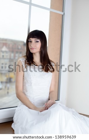 Beautiful bride sitting on the window sill on her wedding day