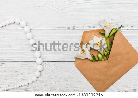Flat lay with White lilies in craft envelope on old white wooden background