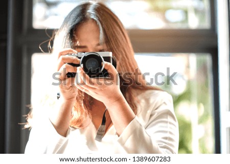 Selected focus, Asian woman Amateur photographer holding a camera and take a photo. in cafe or restaurant.
