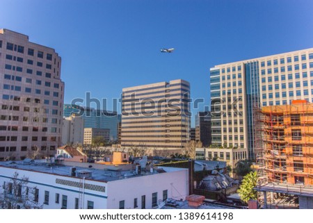 Downtown San Jose cityscape view from San Pedro Market Parking Garage overlooking San Pedro Street and Santa Clara Street with airplane flying overhead.