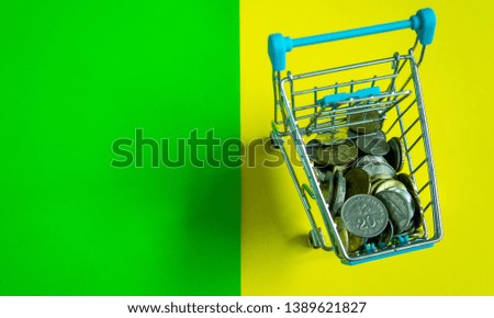 Coins in the shopping cart on yellow and green background.