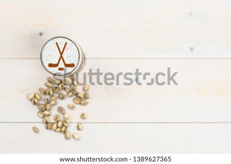 Beer with silhouettes of hockey sticks on beer foam and pistachios on light wooden background. Empty space for text.