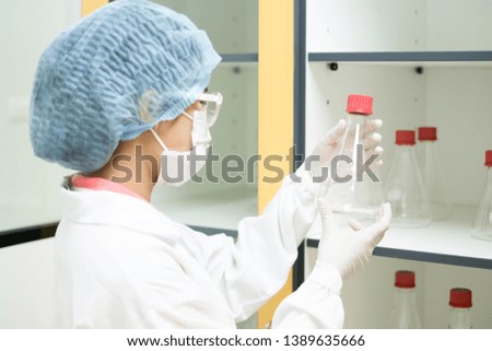 The microbiologist is holding and looking to select the glassware for preparation of laboratory testing in quality control department of pharmaceutical industry.