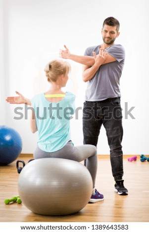 Middle age blond woman exercising on gymnastic ball during session with physiotherapist