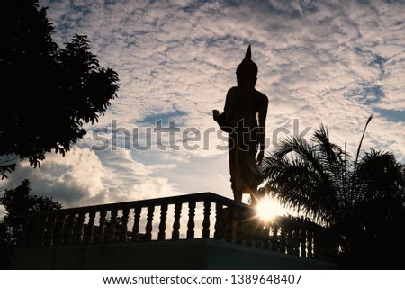 Buddha statue in standing manner   facing to sunset with cloudy blue sky,low angle view.
Outdoor silhouette buddha statue with sunray.