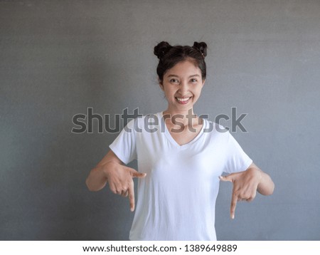 Charming carefree woman with positive expression, points down with both index fingers, dressed in casual clothing, has broad intrested smile, isolated over gray background. Look there, please 