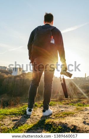 man standing on the top of the hill with camera in hands on sunset. lifestyle concept