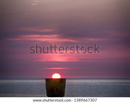 Dunwich, Suffolk, England, Britain, July 2018, sun rising on horizon appearing to come out of bucket on beach