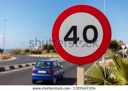 A blue car drives towards a roundabout, the speed is limited to 40 kilometers per hour.