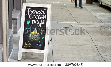 Sidewalk sign advertising French cream puffs with hand drawn illustration on urban sidewalk