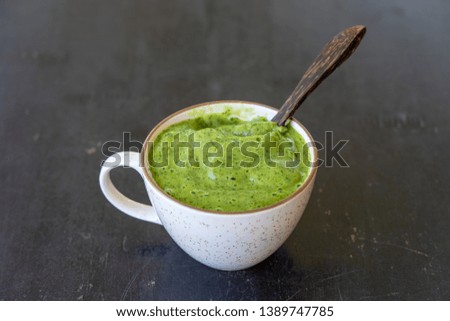 Fresh green smoothie from avocado, banana, parsley, dill and honey in white cup on wooden background, close up. Concept of healthy eating