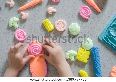 Child's hands with colorful clay. 
ice cream, fruits and vegetables from plasticine. 
Pastel color plasticine. Homemade clay. Close up