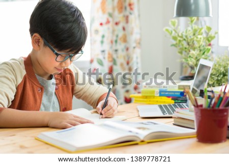 Smart looking Asian teen boy wear glasses, write homework, take notes from online lessons, preparing for the exam due to pandemic of Covid-19 and social distancing. Online Learning Technology. Preteen Royalty-Free Stock Photo #1389778721