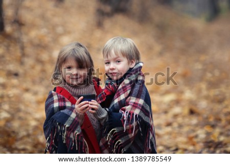 Frozen children in the autumn forest bask under a warm blanket, a boy and a girl warm themselves with tea in the park, cozy pictures for postcards