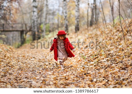 A girl in a red coat and felt hat walks merrily through the autumn forest, golden autumn, childhood and loneliness