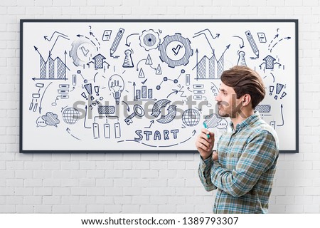 Side view of young man with marker wearing checkered shirt drawing business plan sketch on whiteboard in room with white brick walls. Concept of start up and business education