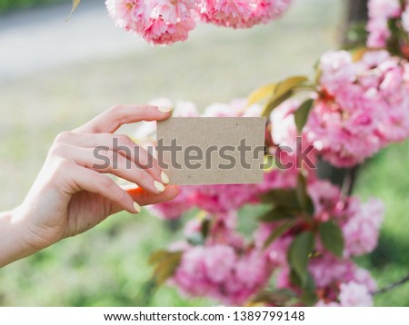 Hand holding a craft business visit card, gift, ticket, pass, present close up on nature background