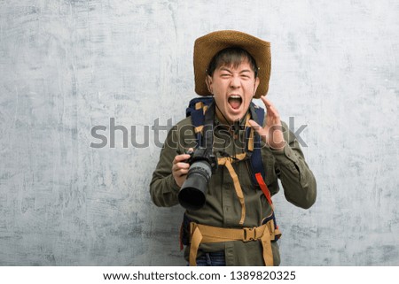 Young chinese explorer man holding a camera shouting something happy to the front