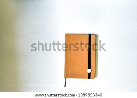 Notebook (beige, brown), lying on a white table, illuminated by natural muted daylight.