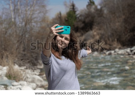 Young beautiful girl on nature takes a selfie on the phone and takes pictures of nature. Good mood on a bright spring day. Tourism and travel.
