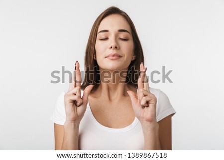Portrait of a beautiful young woman wearing casual clothing standing isolated over white background, holding fingers crossed for good luck