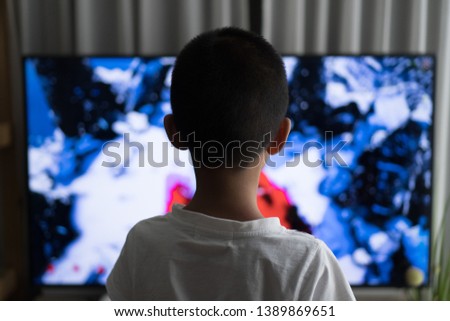 A young boy is watching a television screen with his back for a tv effect on children or a communication concept