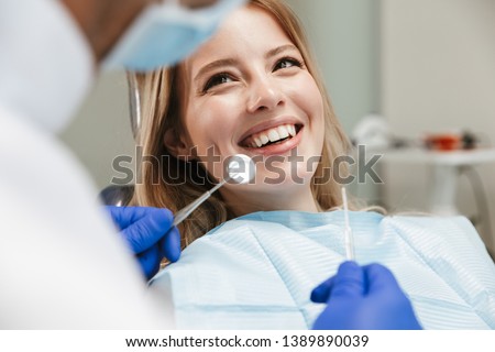 Image of pretty young woman sitting in dental chair at medical center while professional doctor fixing her teeth Royalty-Free Stock Photo #1389890039