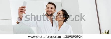 panoramic shot of cheerful man taking selfie while standing with girlfriend in bathroom 