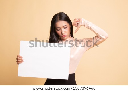 Young Asian woman show thumbs down with white blank sign on  beige background