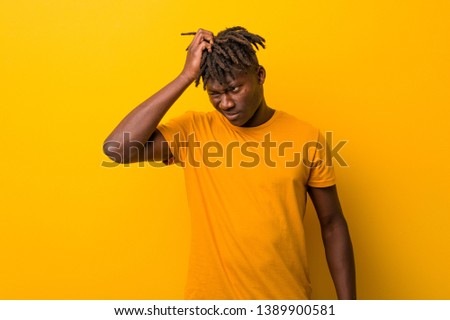 Young black man wearing rastas over yellow background tired and very sleepy keeping hand on his head.