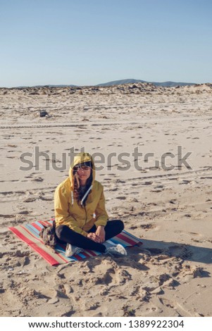 Young and brunette woman with her little dog on the beach with yellow raincoat and cap. Looking at the horizon.