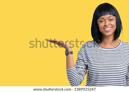 Beautiful young african american woman wearing stripes sweater over isolated background smiling cheerful presenting and pointing with palm of hand looking at the camera.
