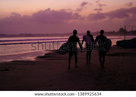 ocean shore at sunset. silhouettes of boats and people. surfers go to the beach. the glow of the setting sun on the sand. twilight. bright multi-colored sky