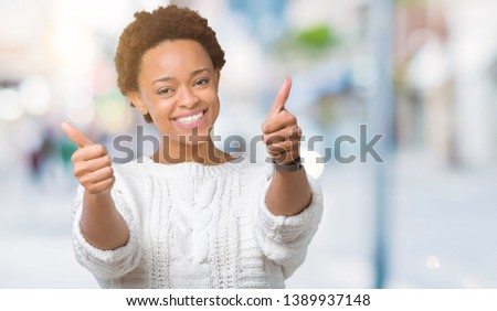 Beautiful young african american woman wearing sweater over isolated background approving doing positive gesture with hand, thumbs up smiling and happy for success. Looking at the camera, winner