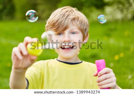 Boy makes soap bubbles and looks at them amazed while hovering in the summer
