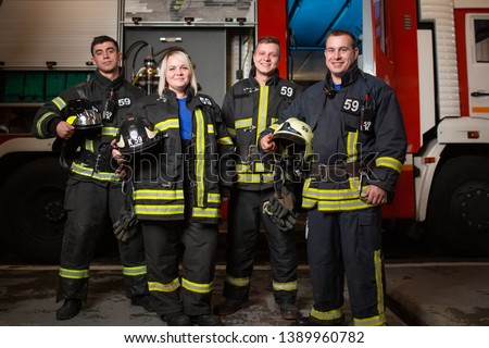 Full-length picture of three young fire men and woman on background of fire truck